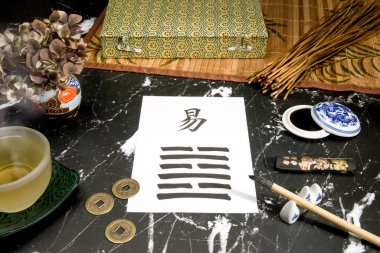 Close up of an I Ching arrangement with the 63th hexagram (After Completition/Chi Chi) written with a chinese ink brush on rice paper. There are also yarrow stalks, a chinese ink tank, a cup of tea and chinese coins on black marble. clipart