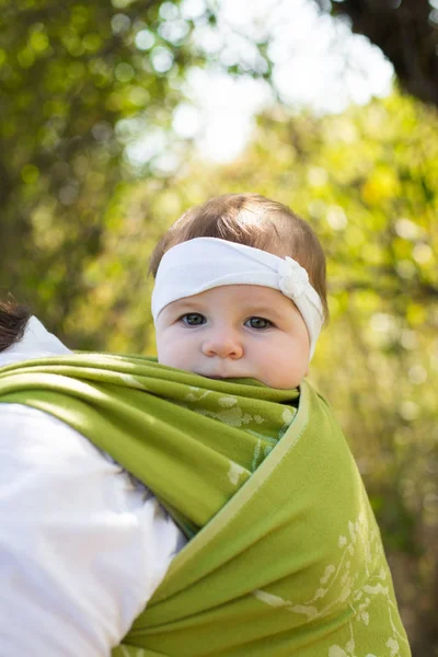 可爱时尚婴儿的画像 穿着绿色帆布婴儿吊袜带 头戴白色头巾 与现代父母一起走在户外 与成人同坐 — 图库照片