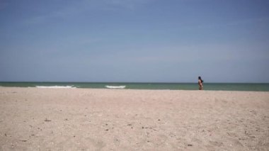 Deniz kumlu sahil manzarası ve siyah bikinili seksi çekici bir kız. Çerçevenin diğer tarafına koşuyor, sportif bir kadın, tatil aktivitesi.