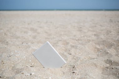 Kumsalda deniz manzaralı beyaz kitap okuyucu tableti, tatilde mükemmel bir eğlence, roman okumak, ders çalışmak ve zevk almak.