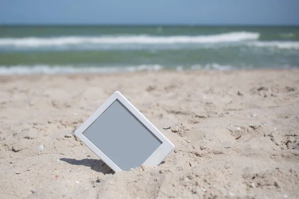 電子書籍リーダータブレット 砂から突き出た灰色の画面の白いフレーム 読書とビーチの休暇のレジャー — ストック写真