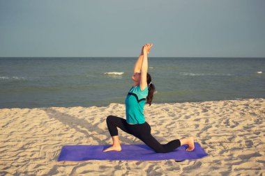 Kadınlar deniz sahilinde spor egzersizleri yapıyor, Anjaneyasana - düşük hamlede eller havada, yoga fitness pratiği açık havada, sabah tatili egzersizleri