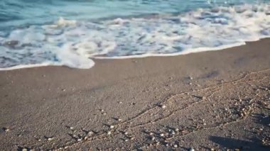 Yaklaşan mavi deniz dalgaları ve kabuklu ıslak kum, tatil konsepti.