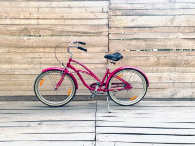 Pembe kruvazör kadın bisiklet standı ahşap arka planda, şehir bisikleti sürüyor. 