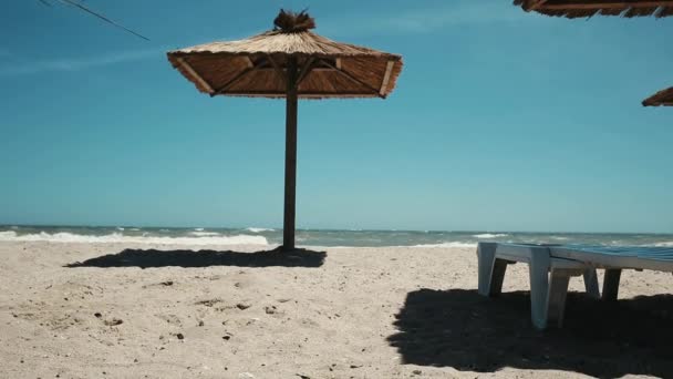 海の景色と波 休日の概念を砂でわら傘とプラスチック製のチェイスラウンジで空のビーチリゾートの景色 — ストック動画