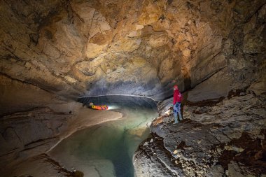 CERKNICA, SLOVENIA - 7 Haziran 2020: Krizna Jama karst mağarasındaki büyük bir mağarada yer altı gölünün üzerinde duran bir mağara bilimci