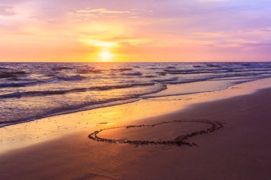 Sunse kumlu bir plaj üzerinde çizilmiş kalp şekli