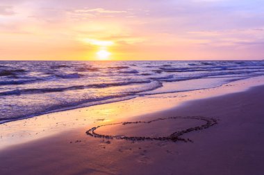 Sunse kumlu bir plaj üzerinde çizilmiş kalp şekli