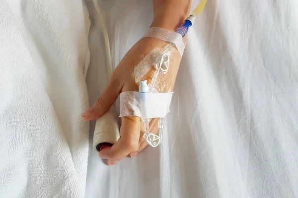Close-up of patient hand with infusion needle and IV tube for intravenous infusion pushing emergency button at bed.