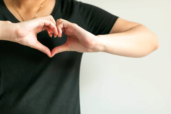 A woman use hands display love symbol by splice fingertips together to be heart shape place at front of left chest. — Stock Photo, Image