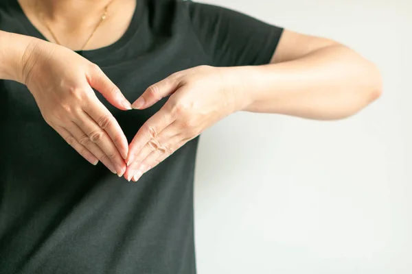 A woman use hands display love symbol by splice fingertips together to be heart shape at front of left chest. — Stock Photo, Image