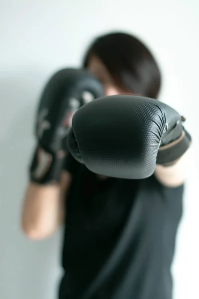 Una mujer con guantes de boxeo negros estirando su puño izquierdo hacia el blanco delantero . —  Fotos de Stock