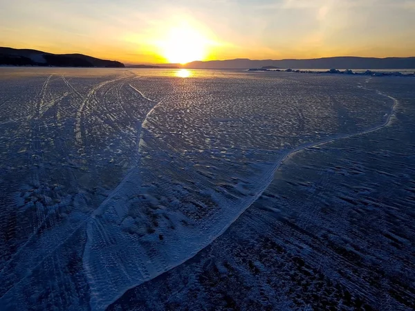 Bela cena do pôr do sol do Lago Baikal no inverno; com textura e padrão pitoresco de marcas de pneus na superfície do gelo . — Fotografia de Stock
