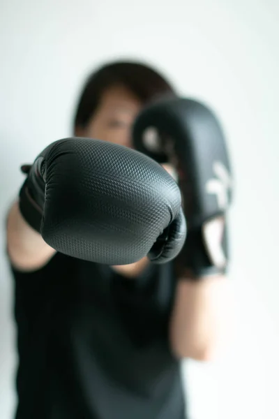 Una mujer con guantes de boxeo negros estirando su puño derecho hacia el blanco delantero . —  Fotos de Stock