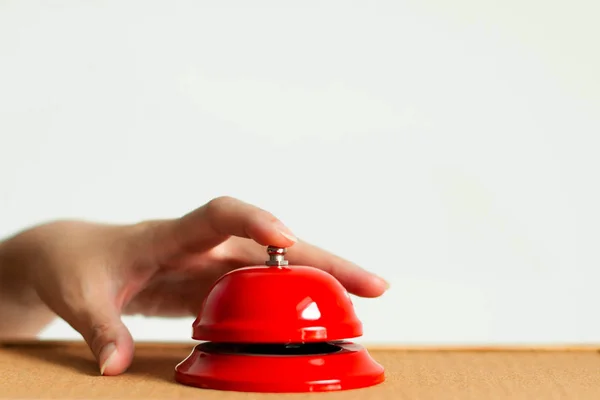 A hand using index finger pressing the bell button of red vintage style handbell on wooden surface in close-up.