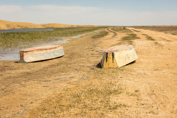 Un barco al revés. Botes de remos en las cañas. Barco de madera en una orilla de lago cubierta de hierba en un día de verano. Mar de Aral, Kazajstán — Foto de Stock