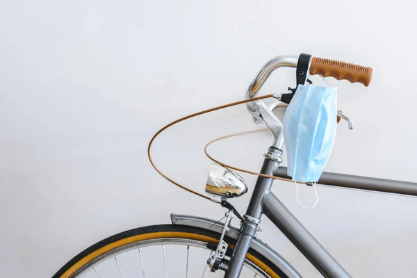 blue surgical mask hanging from the handlebar of a vintage bike. Concept of new normality after pandemic. Selective focus