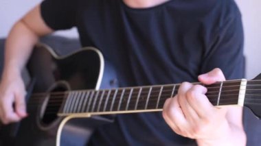 Beyaz bir adam siyah akustik gitarla akor çalıyor. Sol ele seçici odaklanma