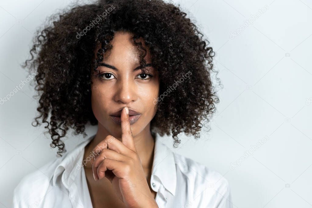 beautiful afro-american woman doing gesture of silence with finger in lips with white background