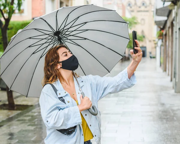 Kızıl saçlı genç bir kadın yağmurlu bir günde telefonla fotoğraf çekiyor.