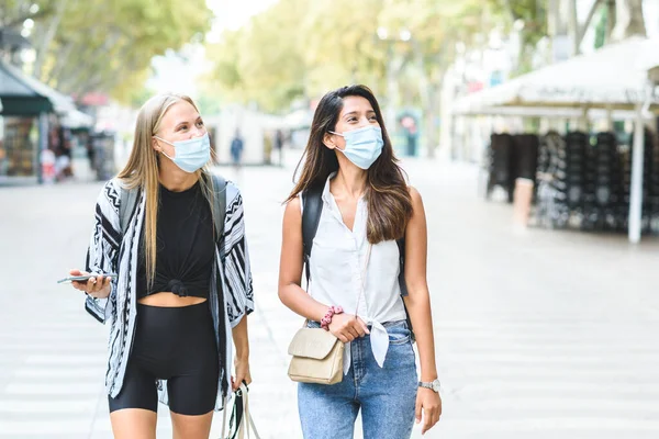 Mavi koruyucu maskeler takan ve Barselona sokaklarında günlük giysiler giyen iki genç bayan turist.