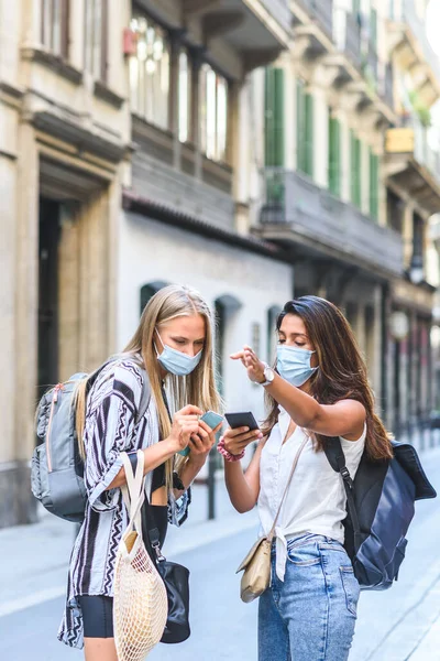 young indian female tourist helping other caucasian tourist to find an address with the help of an smart phone