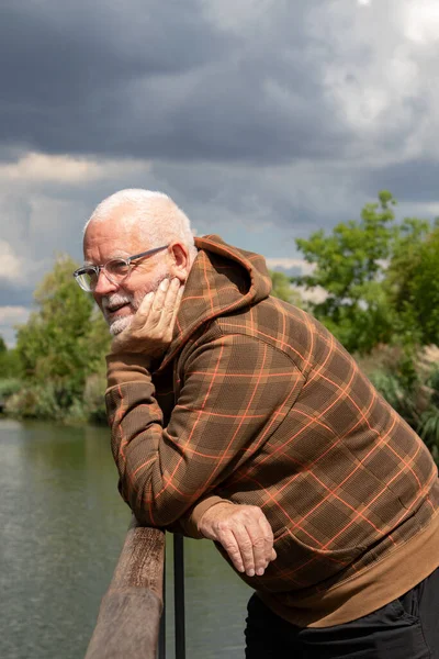 Elderly gray-haired man thinks, smiling at a river