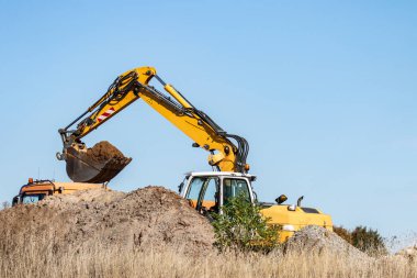 Bir kazıcı bir kamyona kum tarıyor.