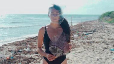 Kafasında şeffaf plastik bir torba ve elinde ölü bir ağılla Karayip sahilinde yosun ve çöp dolu bir kız.