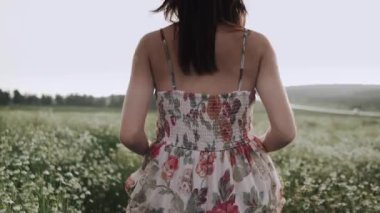 Elbiseli bir kız gün batımında papatya tarlasında koşuyor.