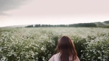 Gün batımında küçük kız papatyaların arasında koşar