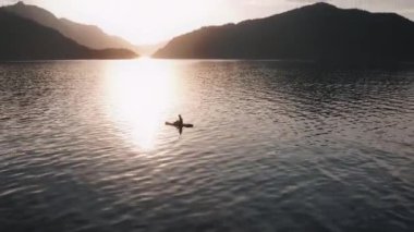 Gün batımında gölün ortasında mayo giymiş bir kız Altai 'deki dağların arka planında yüzer.