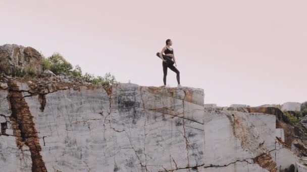 黎明时分 一个穿着运动服 手里拿着地毯的女孩站在石崖上 — 图库视频影像