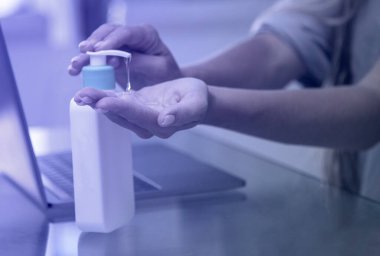 Kadın antiseptik kullanıyor. Evde bir dizüstü bilgisayar üzerinde çalışıyorum. Mavi renk