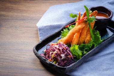 Ahşap masa arkasında siyah bir tabakta kızarmış panko karidesleri. Hindistan cevizli karides, salata, garnitür, sebze ve acı biber sosuyla karıştırın. Asya restoranı. Kapat, boşluğu kopyala