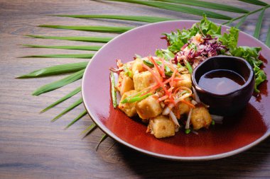 Kızarmış tofuyu ahşap masa arkasında kırmızı bir tabakta karıştır. Salata ve soslu sağlıklı Asya yemeği. Restoran menüsü. Kapat, boşluğu kopyala