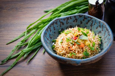 Ahşap arka planda bir kasede kızarmış pirinç. Geleneksel Asya usulü yumurta ve sebzeli pilav. Sağlıklı, vejetaryen yiyecekler. Restoran menüsü. Kapat, boşluğu kopyala