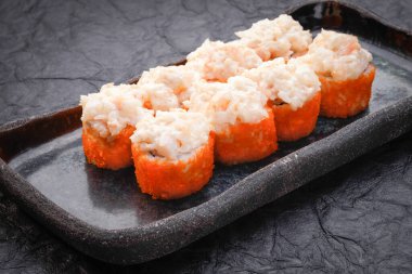 Suşi seti koyu arka planda servis edilir. Fırında makarna, masago, somon, krem peynir, avokado ve karidesli Philadelphia maki. Çeşitli suşiler. Japon yemeği. Restoran menüsü. Yan görünüm, kapat