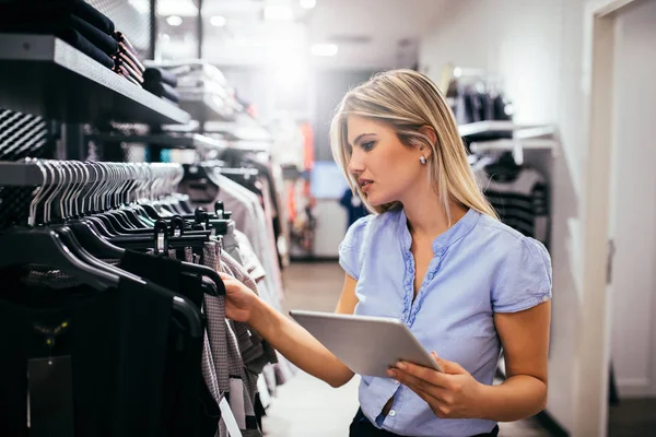 デジタル タブレットを使用して 衣料品店で買い物中の若い女性 — ストック写真