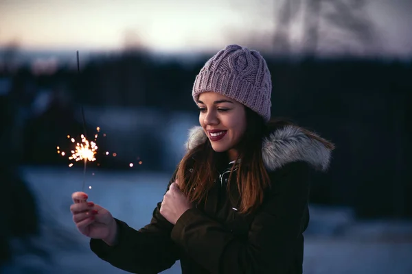 Portrait of young woman holding a sparkling stick outdoors.