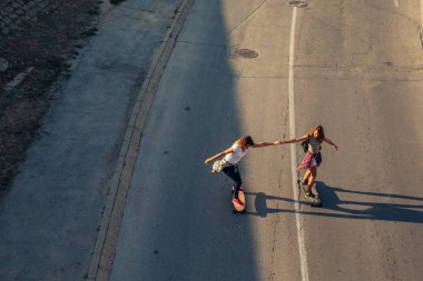 İki genç kız onların longboards sürme el ele.