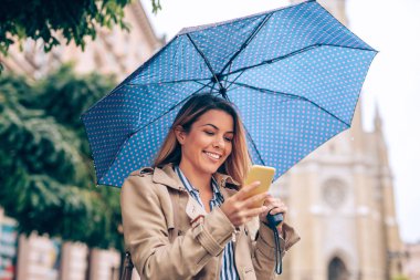 Yağmur durdurmak beklerken telefonunu kullanan bir genç güzel kadın.
