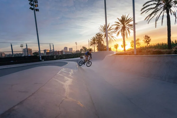 A young man performing a jump on his BMX in a sunset-lit bowl.