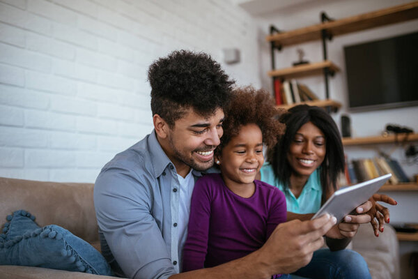 Happy black parents are teaching their daughter by using a tablet.