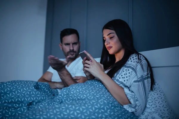 A young husband is angry at his wife for constantly using her phone in bed.