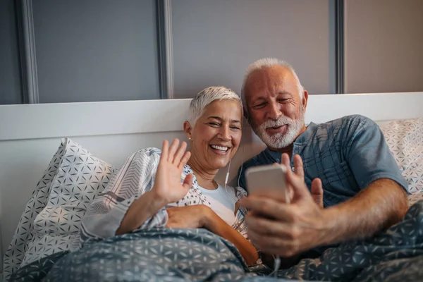 年配のカップルは 自分の携帯電話上の音楽を聴きながらイヤホンを共有します — ストック写真
