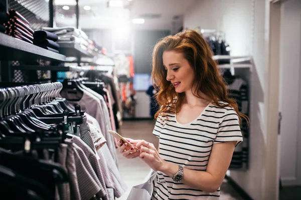 衣料品店で携帯電話を使用して若い女性を笑顔 — ストック写真