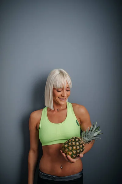 A young athletic woman holding a ripe pineapple.