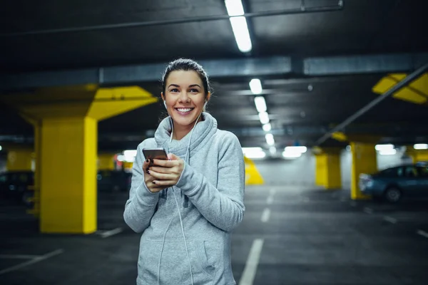 Portrait Smiling Athlete Woman Using Mobile Phone Underground Car Parking — Stock Photo, Image