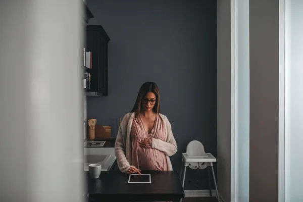 Беременная Женщина Проверяет Свой Планшет Тускло Освещенной Кухне Утром — стоковое фото
